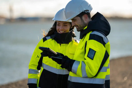 Two workers in hi-vis jackets and hard hats reviewing tablet at outdoor work site